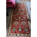 A Caucasian rug decorated stylised floral designs on a red ground with main ivory border stripe,