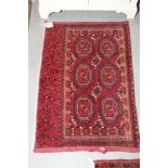 A Bokhara rug decorated six octagonal guls with a candlestick on a red ground with a candlestick