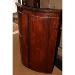 A George III wall hung mahogany bowfront corner cupboard, door inlaid oval paterae of oak leaves