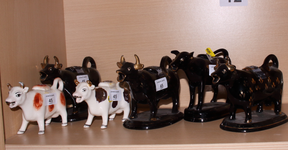 Four black and gilt decorated cow creamers and two others