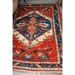 A Kazak rug decorated blue and ivory hexagonal medallion on a red ground with three border