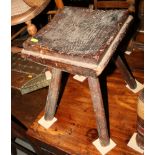 A rectangular rustic wooden stool with dished seat, on four splayed supports