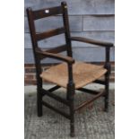 An oak ladder back elbow chair with rush envelope seat, on turned and stretchered supports