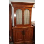 A grained pine bookcase, the upper section enclosed two arch top glazed doors over cupboards, on