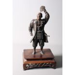 A mid 20th century Japanese bronze model of a standing samurai, with his hand aloft, on a pierced