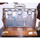 A late Victorian oak three-bottle tantalus with white metal carrying handle, complete with cut glass