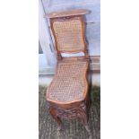 A French 19th century carved walnut bidet stool with cane seat and back panel and Rouen faience