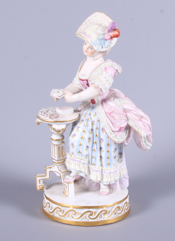 A late 19th century Meissen porcelain figure of a standing woman in 19th century costume by a tripod