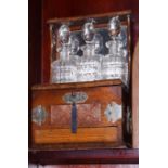 An Edwardian carved oak integrated tantalus/cigar twin-handled box with three cut glass decanters,