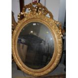 A carved giltwood framed oval wall mirror with bevelled plate and ribbon surmount, plate 21 1/2" x