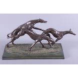 A bronzed Art Deco design figural group of three running and leaping greyhounds, on a painted wooden