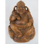 A carved bamboo figure of a seated gentleman holding his belt in one hand,