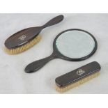 An early 20th century ebony backed mirror and two brushes,