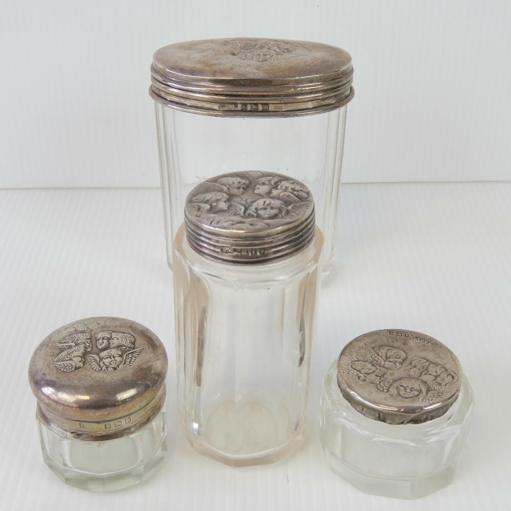 Four HM silver topped faceted glass dressing table pots, each with repoussé cherub design.