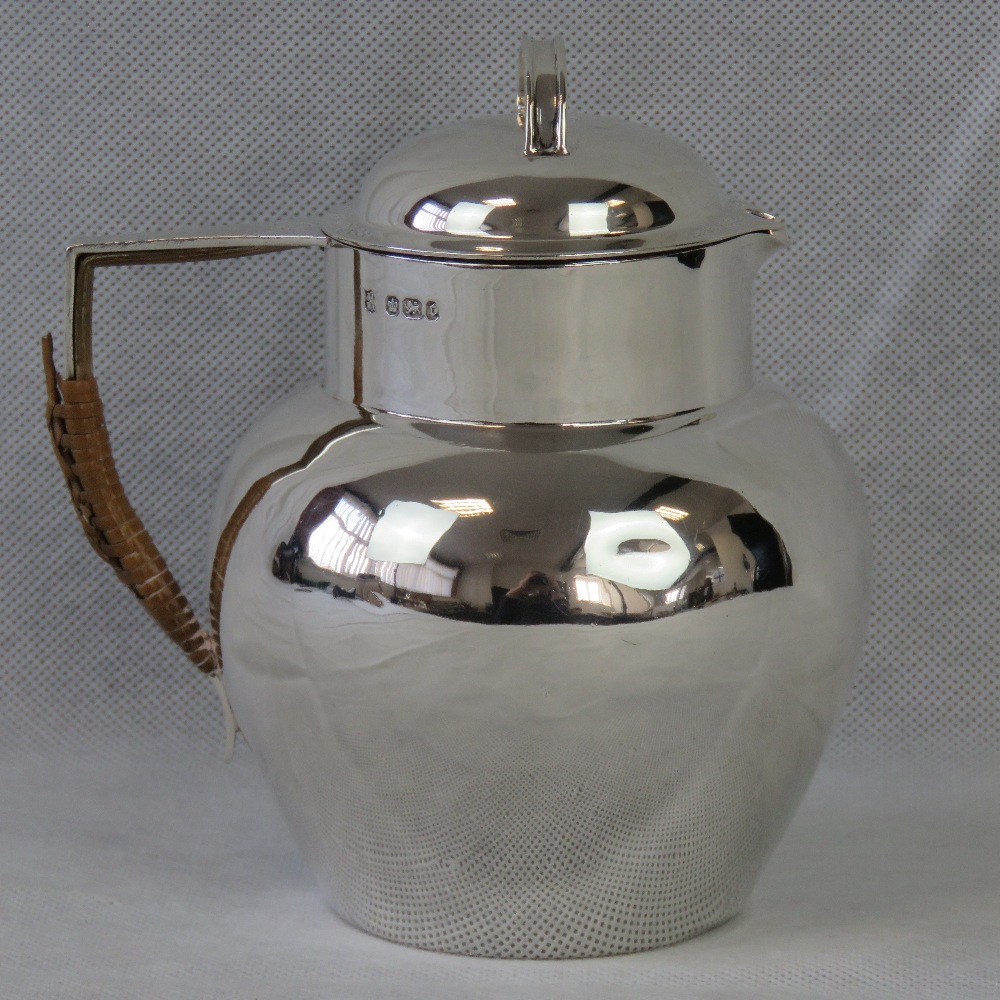 A HM silver Arts and Crafts hot water jug with wicker covered handle,