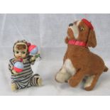 A wind-up jumping dog, together with a wind-up rattle-shaking wax bodied baby.