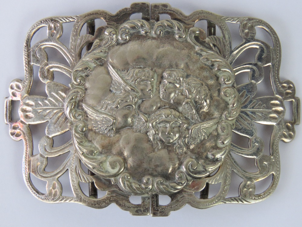 A large white metal belt buckle, central circular plaque with repoussé depiction of cherubs,