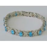 A tennis bracelet set with oval blue stones separated by small white stones set in an x shaped