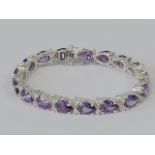 A silver tennis bracelet set with teardrop shaped purple stones separated by pairs of small white