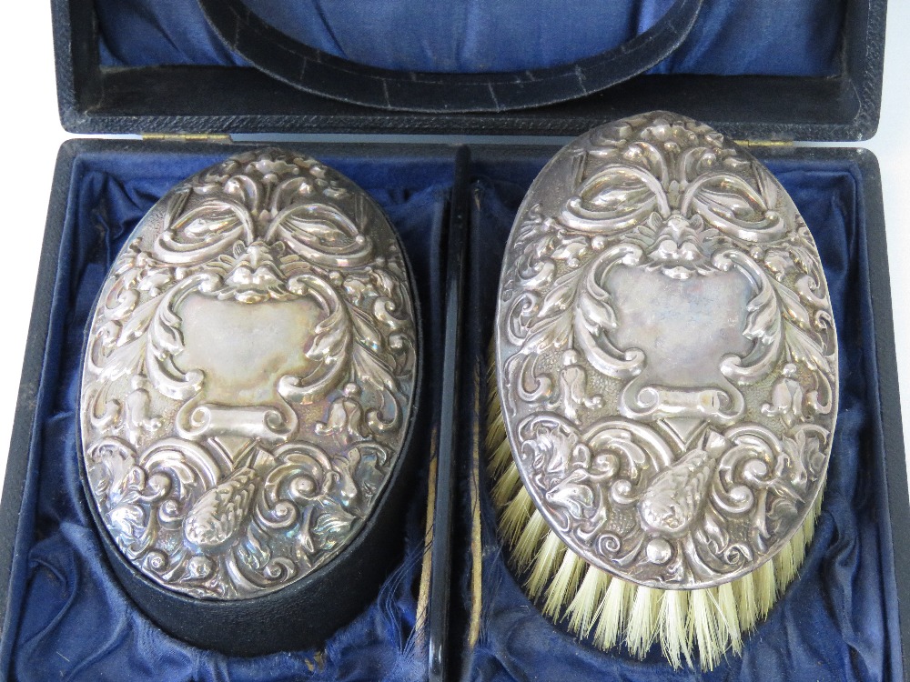 A pair of HM silver brushes within original fitted case, repoussé scrolling vines,