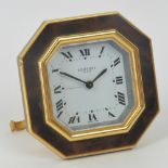 A Cartier travel alarm clock, gilt metal and tortoise shell effect case with hinged stand,