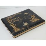 A Japanned papier mache black ground album containing a large quantity of hand tinted early 20th