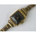 An 18ct gold ladies manual wind wristwatch on 9ct gold strap, Swiss movement with black dial,