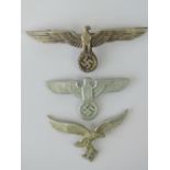 Three WWII German cap badges each depicting eagle and swastika; two stamped 'A' to back,