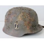 A WWII German helmet, later camo painted and applied double decal, leather lining and chin strap.