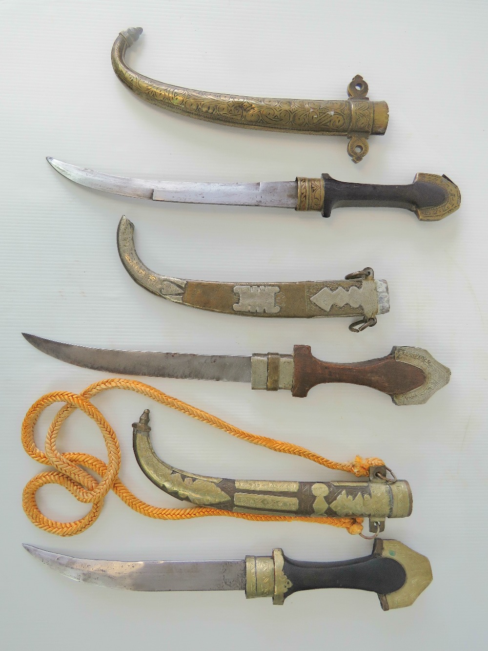 Three souvenir Jambiya daggers each with brass curved scabbard, wooden grip and brass pommel.