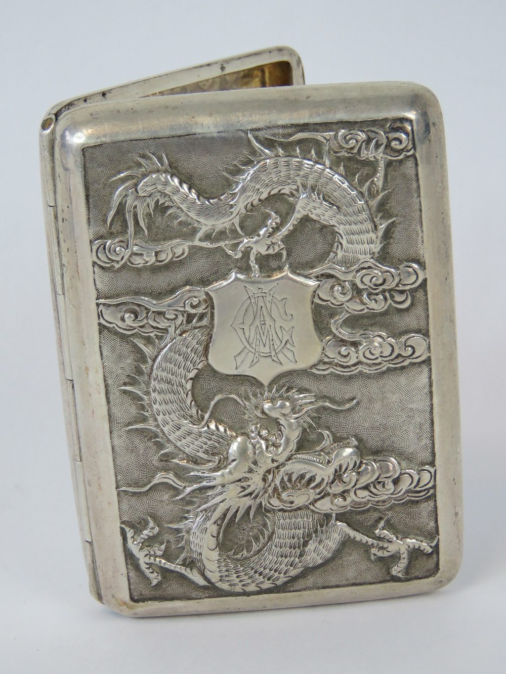 A Chinese white metal cigarette case featuring a repoussé four-toed dragon encircling an engraved