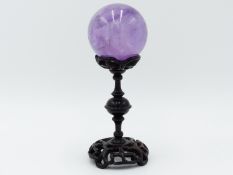 AN ORIENTAL CARVED AND PIERCED HARDWOOD STAND SUPPORTING A POLISHED QUARTZ CRYSTAL BALL 15 CM HIGH