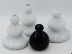 THREE VICTORIAN WHITE GLASS DOOR STOPS 17CM TALL TOGETHER WITH A SMALLER BLACK GLASS EXAMPLE.