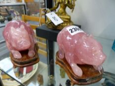 A PAIR OF CHINESE PINK ROSE QUARTZ TYPE MODELS OF RECUMBENT CATS ON HARDWOOD STANDS. 11CM LONG X 8CM