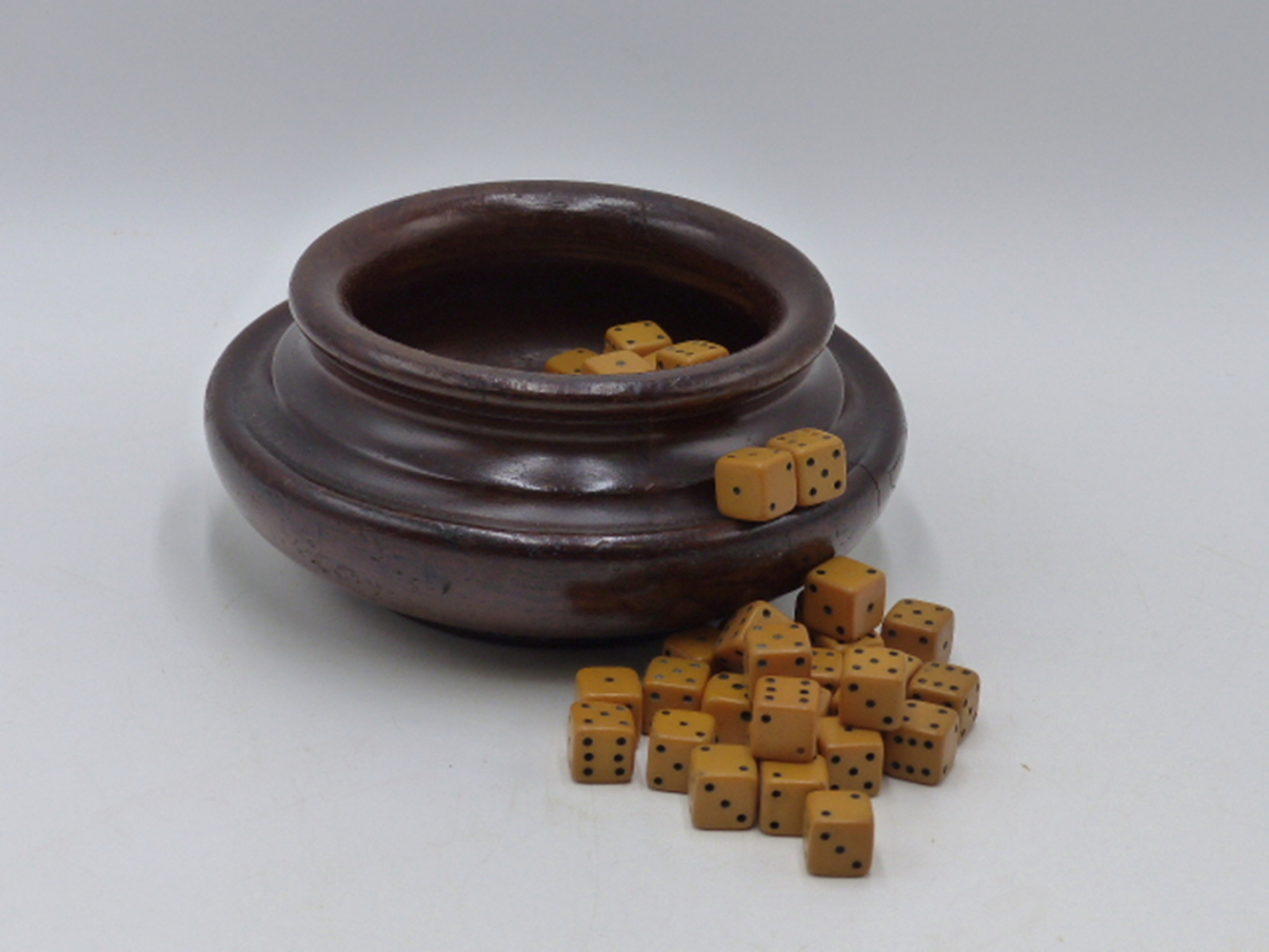 A TURNED MAHOGANY BOWL CONTAINING A LARGE QUANTITY OF GAMING DICE.