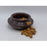 A TURNED MAHOGANY BOWL CONTAINING A LARGE QUANTITY OF GAMING DICE.