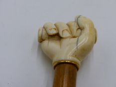 A 19TH CENTURY IVORY TOP WALKING CANE, THE KNOP CARVED AS HAND GRIPPING A STAVE, YELLOW METAL RING