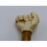 A 19TH CENTURY IVORY TOP WALKING CANE, THE KNOP CARVED AS HAND GRIPPING A STAVE, YELLOW METAL RING