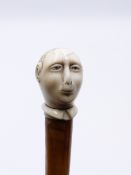 AN INTERESTING COLONIAL WALKING CANE WITH LEATHER RING SHAFT, HORN HANDLE AND CARVED IVORY KNOP IN