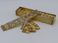 A 19TH.C.SET OF BONE DOMINOES CONTAINED IN A CARVED AND PIERCED SLIDING TOP BOX.