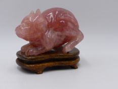 A CHINESE CARVED ROSE QUARTZ FIGURE OF A CROUCHING BEAST ON CONFORMING HARDWOOD STAND.