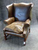 A MAHOGANY GEORGIAN STYLE WING ARMCHAIR COVERED IN STUDDED BROWN LEATHER.