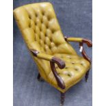 A CARVED MAHOGANY VICTORIAN STYLE ARMCHAIR WITH BUTTONED OLIVE GREEN LEATHER ON BRASS CASTORS.