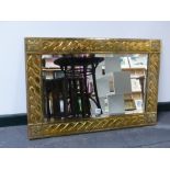 A BRASS ARTS AND CRAFTS MIRROR WITH BEVELLED PLATE AND SPIRAL TWIST DECORATED FRAME. 57x84cms.