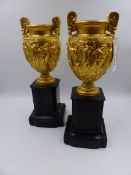 A PAIR OF 19th.C. GILT METAL CLASSICAL STYLE TWIN HANDLE URNS AFTER THE ANTIQUE WITH SHAPED BLACK