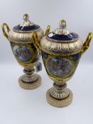 A PAIR OF BERLIN PORCELAIN TWO HANDLED LIDDED PEDESTAL VASES WITH HAND PAINTED GENRE SCENES. H.