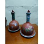 A NEAR PAIR OF TERRACOTTA LIDDED BOTTLE VASES WITH STAND DISHES DECORATED WITH CHINOISERIE SCENES.