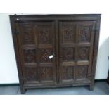 AN EARLY CARVED OAK PANELLED DOOR CUPBOARD WITH SHELVED INTERIOR.