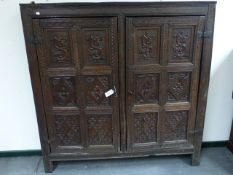 AN EARLY CARVED OAK PANELLED DOOR CUPBOARD WITH SHELVED INTERIOR.