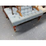 A LARGE BUTTON UPHOLSTERED STOOL ON TURNED LEGS WITH BRASS CASTERS.